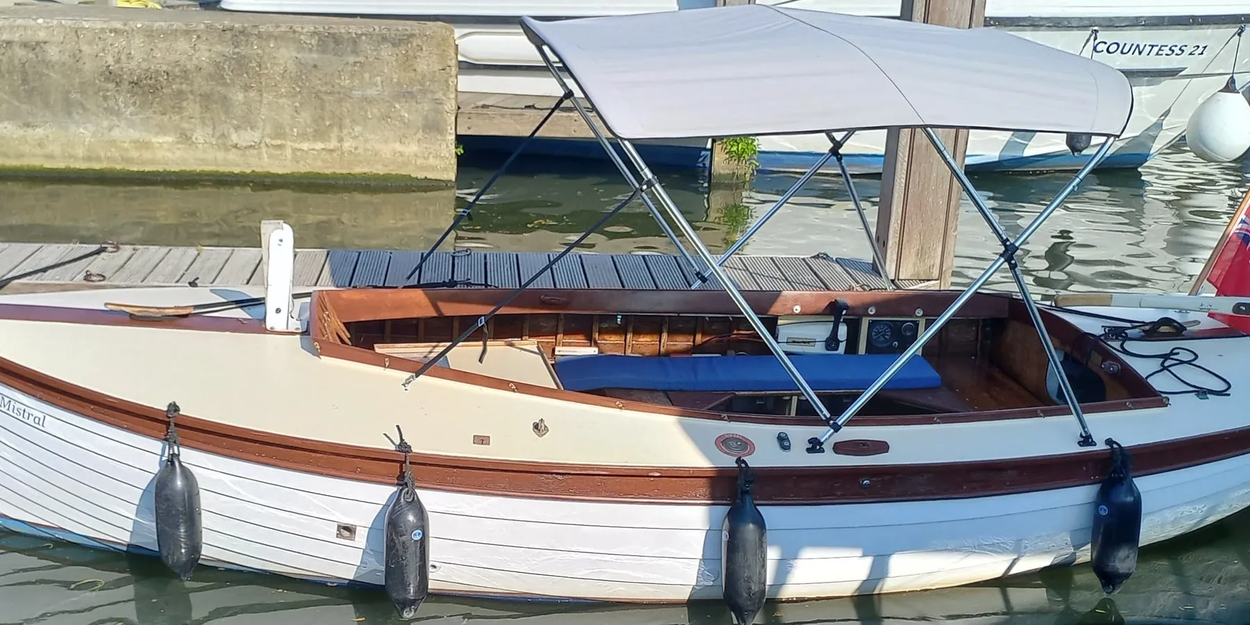 Mistral at the pontoon, cream hull with a varnished mahogany gunwale and a canopy