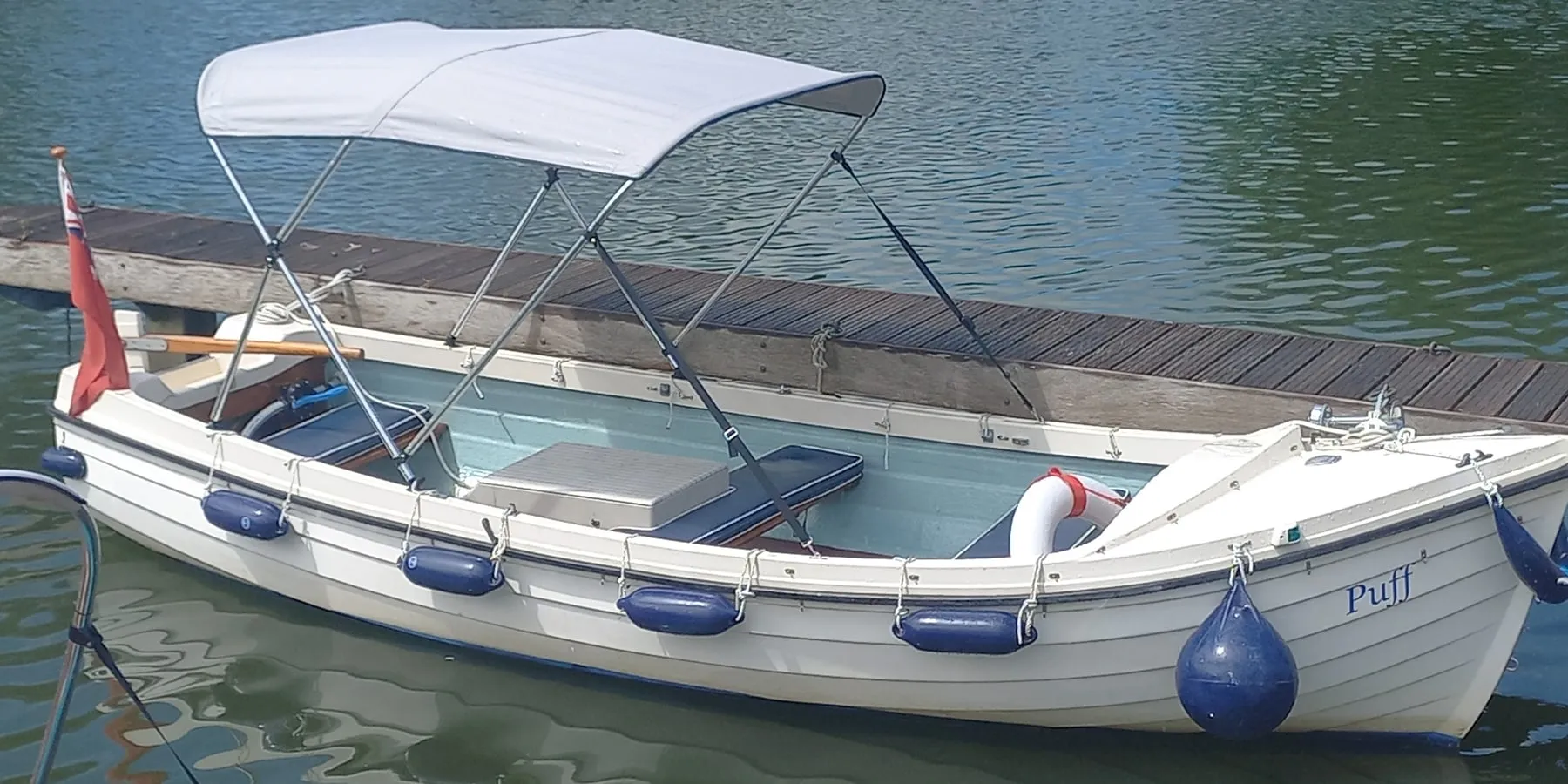 Puff at the pontoon under her white canopy, blue fenders along the hull